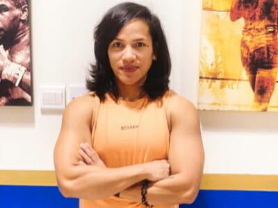 A woman in an orange tank top standing in front of paintings, training as a boxing coach.