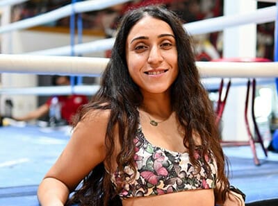 A boxing coach woman posing in a boxing ring for a photo.